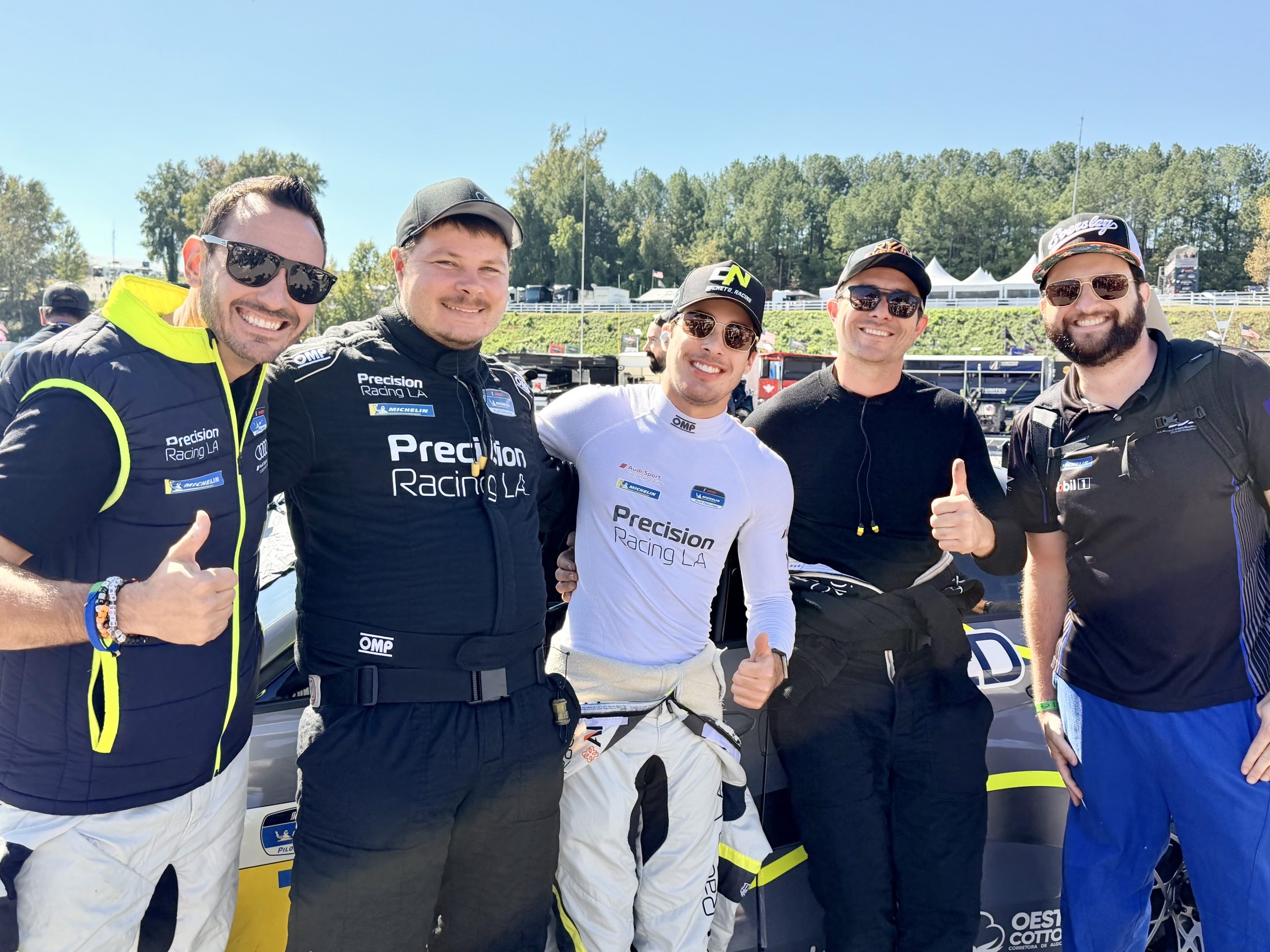 Five men smiling in front of a race car